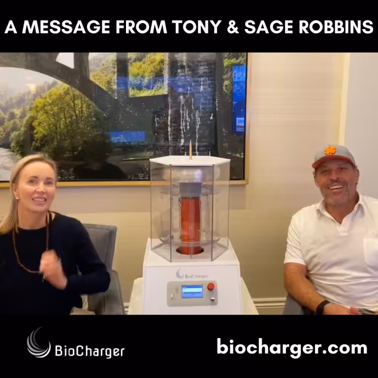 Sage and Tony Robbins Sitting and Smiling with BioCharger Device Between Them