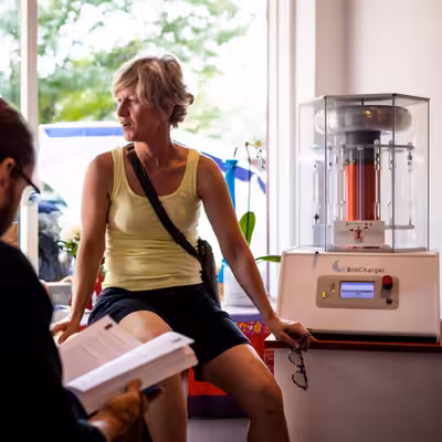 Ewa Long Owner of Aesthetics with Energy Sitting and Smiling In Front of the BioCharger Device