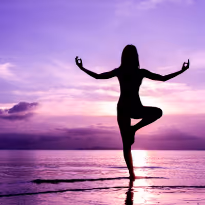 Woman Performing Yoga on the Beach while Looking at the Beautiful Purple Sunset that Reflects on the Sea