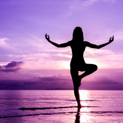 Woman Performing Yoga on the Beach while Looking at the Beautiful Purple Sunset that Reflects on the Sea