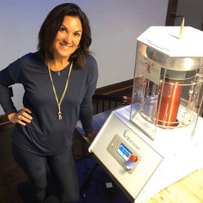 Female Owner of BKS Yoga Studio Smiling and Standing Next to the BioCharger Device