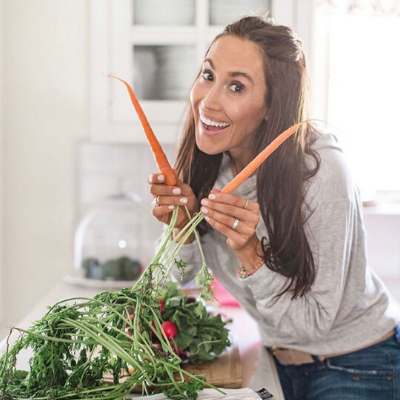 Female Wearing Grey Hoodie in Kitchen Smiling and Posing While Holding Two Carrots