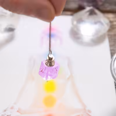 Hand Holding Pendulum Over Drawing Of Female Body With Chakras