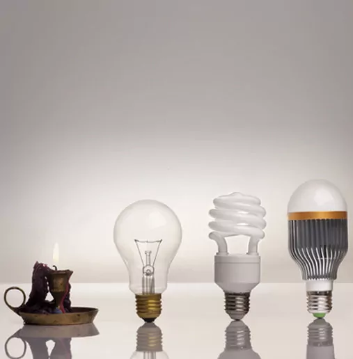 Evolution of a Light Source From Candle to Three Different Light Bulbs on a Grey Background