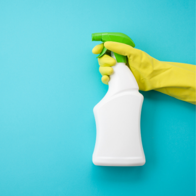 Hand in a Yellow Cleaning Glove Holding Up Cleaning Spray In Front of Blue Wall