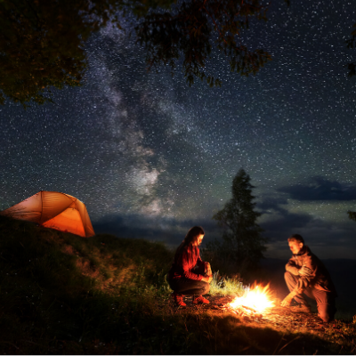 Man and Woman Camping in Mountains and Sitting Around Fire Under Sky Full of Stars
