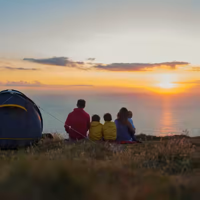 Family Sitting on Grass Beside Blue Tent and Looking in the Beautiful Sunset above the Sea