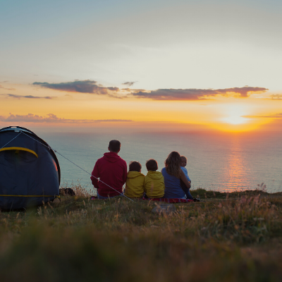 Family Sitting on Grass Beside Blue Tent and Looking in the Beautiful Sunset above the Sea