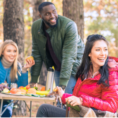Group of People Sitting Around the Table in Nature and Eating Fruits While Looking in the Distance and Smiling