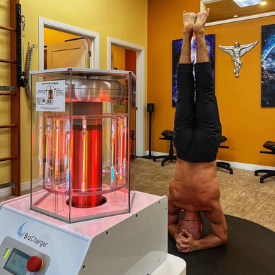 Man Standing on His Head Behind the Working BioCharger Device In The Life Center Chiropractic