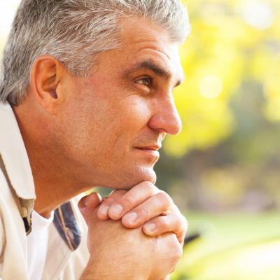 A Man in a Beige Shirt Holds His Hands Under His Chin as He Stares into the Distance and Smiles at it