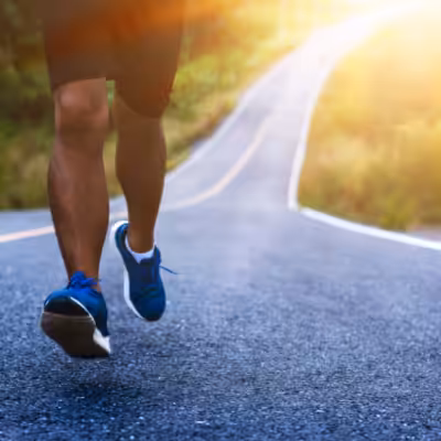 Man in Black Shorts and Blue Sneakers Runs on a Path Surrounded by Grass