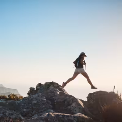 Woman with Black Backpack and Hat Hiking on the Rocks