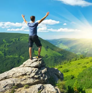 A Man on a Rock With Two Hands in the Air Looking at the Mountains and the Beautiful Sunny Sky