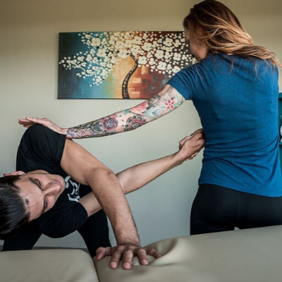Woman Performing Stretch Therapy on a Man While he Standing Next to a Stretching Table