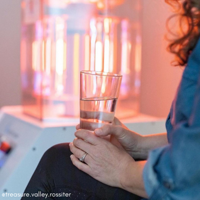 Woman Sitting Next to a Working BioCharger Device and Holding Her Glass of Water in Her Hands