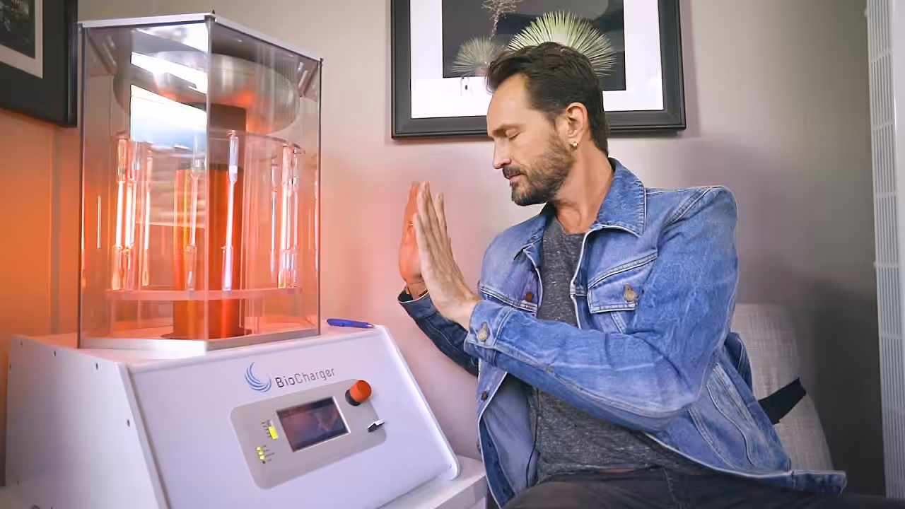Luke Story Closed Eyes Sitting With His Hands Up and Palms Facing Working BioCharger Device