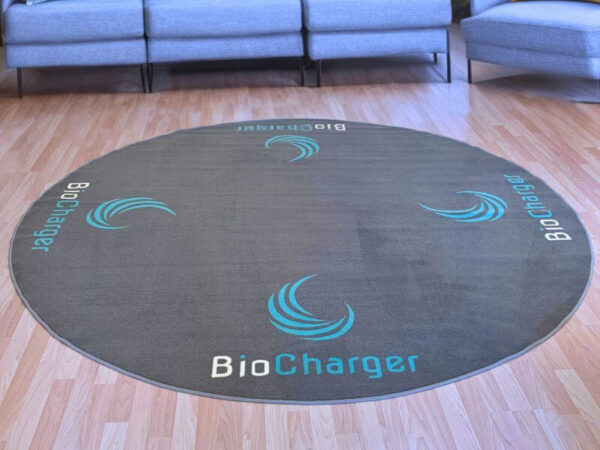 round grey rug with a blue and white BioCharger logo on it with a grey couch in the background