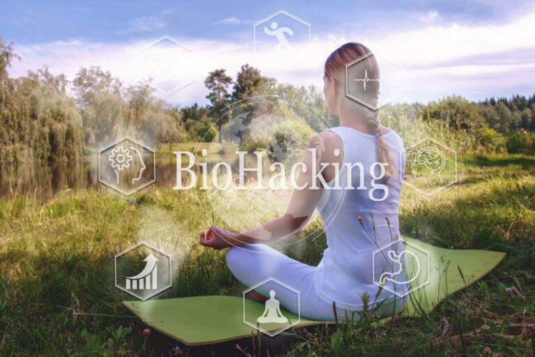 Woman in White Meditating on the Grass Near the Water With a BioHacking letters in the Foreground