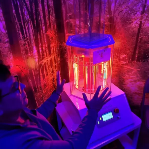 Person in black glasses sitting with their hands up near a glowing vertical health optimization device with a forest backdrop