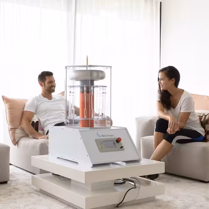 A man and a woman seated in a modern living room, smiling and engaging in a lively conversation with a cutting-edge home device placed on a coffee table between them.