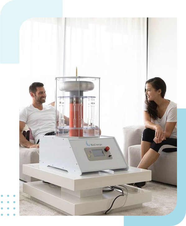 A couple sits relaxed on a couch, smiling at each other, with a table top health optimization equipment between them, suggesting a comfortable home environment intertwined with scientific endeavor or interest.