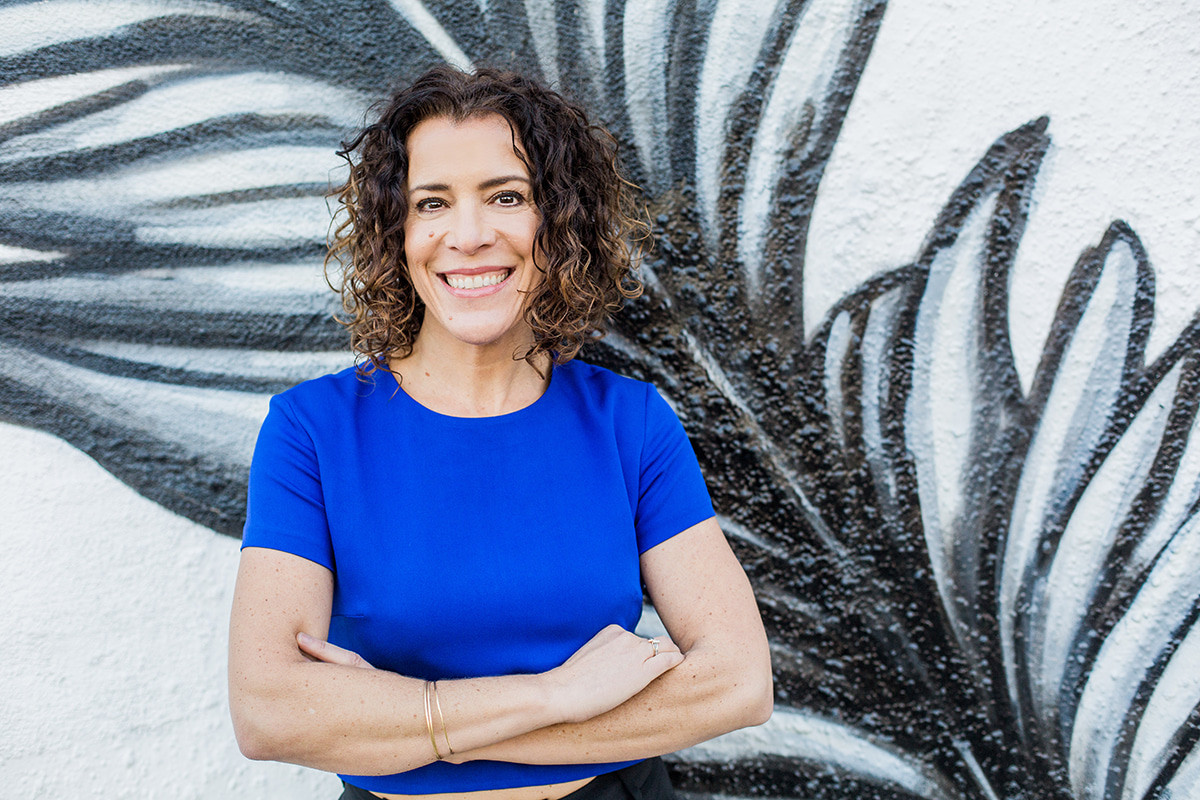 Smiling women with curly brunette hair in front of a large drawing of a leaf